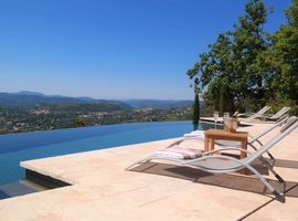 Sunloungers on a stone terrace next to a long infinity pool with panoramic views of the of l'Esterel towards the Bay of Cannes.